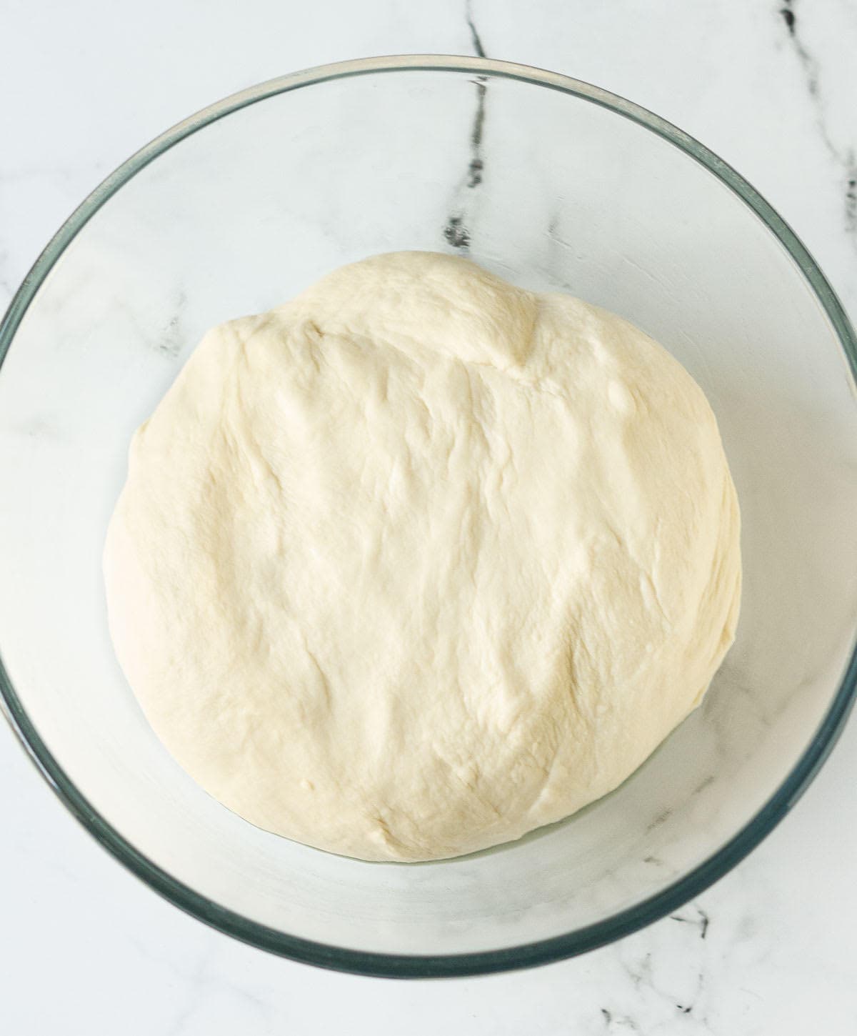 ready dough ready for proofing in a glass mixing bowl.