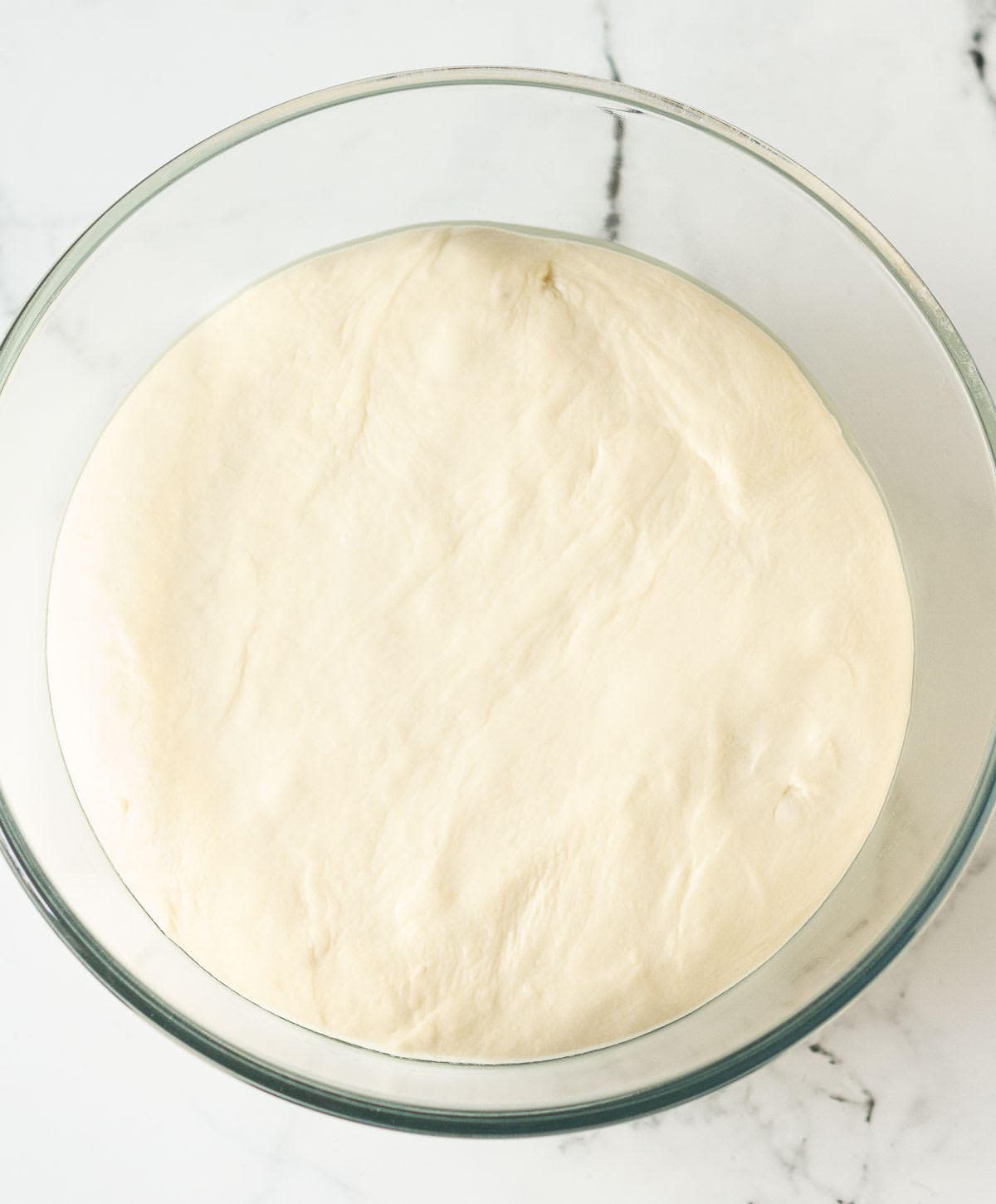 Proofed pretzel dough in a glass bowl.