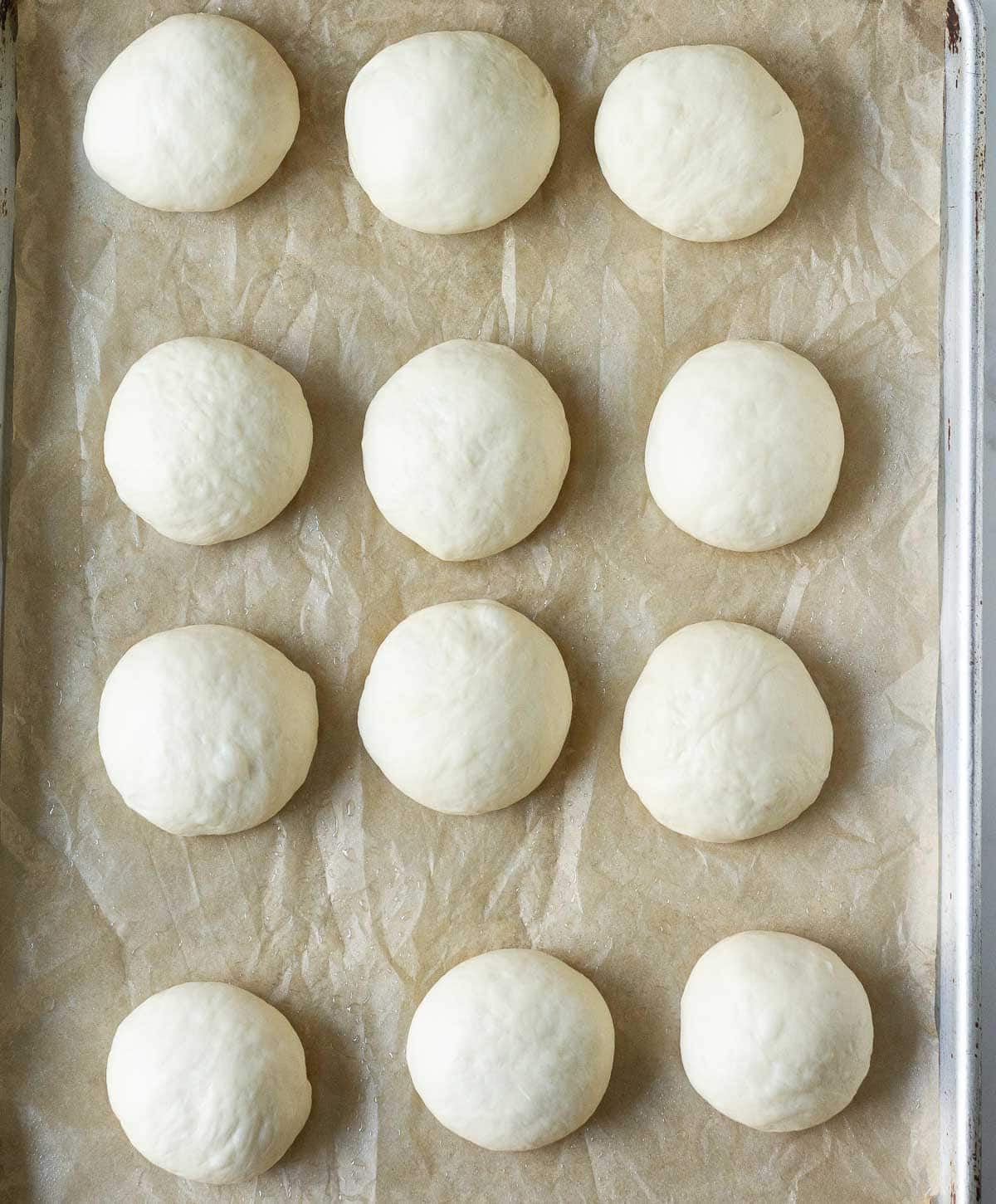 12 dough balls on parchment paper on a baking tray.
