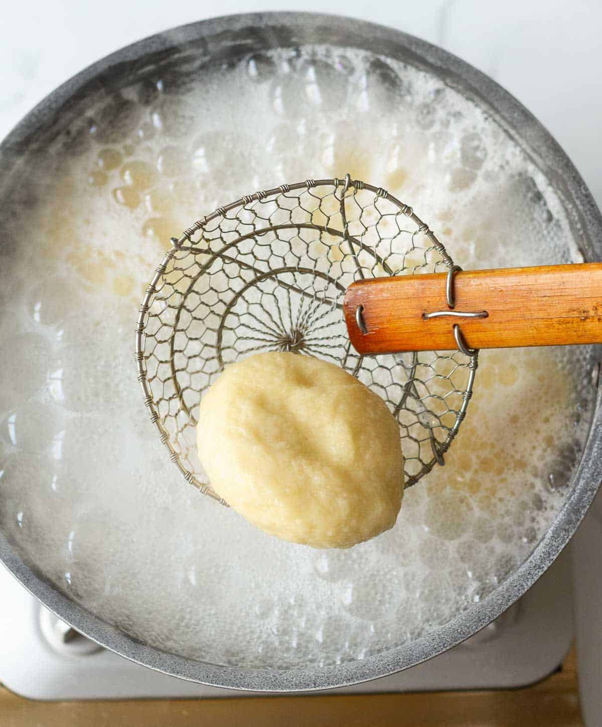 taking a boiled pretzel ball in a spider from a wok full of boiling water.
