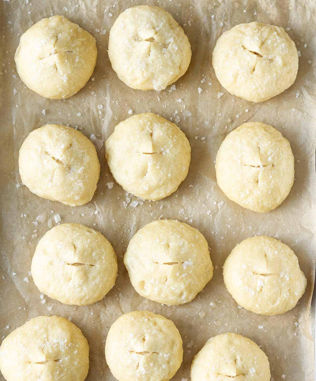 12 dough balls scored and with salt on top on parchment paper lined tray.