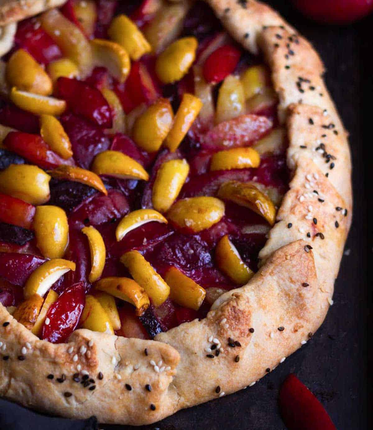A galette with sesame seeds on its crust and filled with plums and apricots.