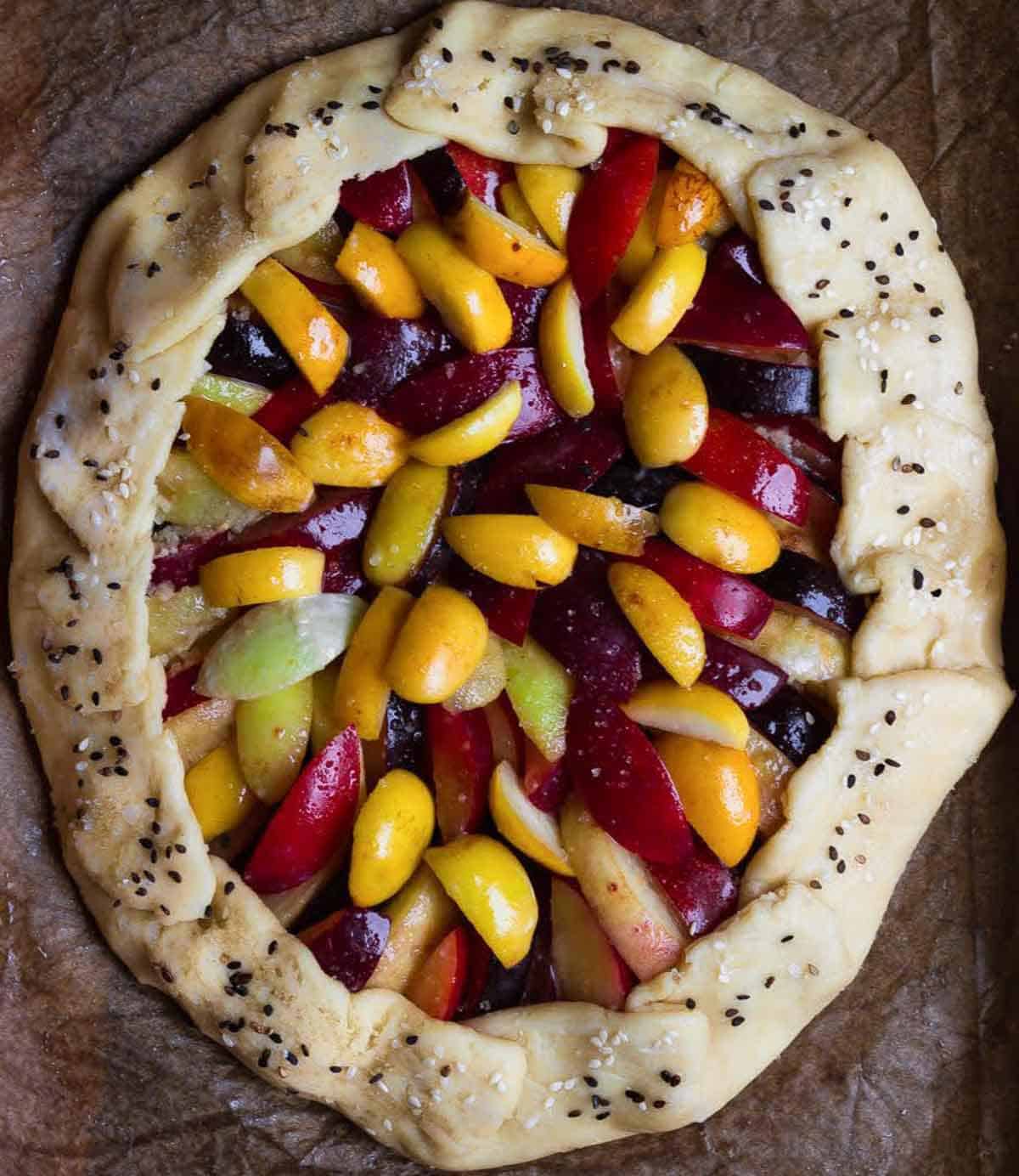 Fruits on pastry dough folded over them, and topped with sesame seeds.