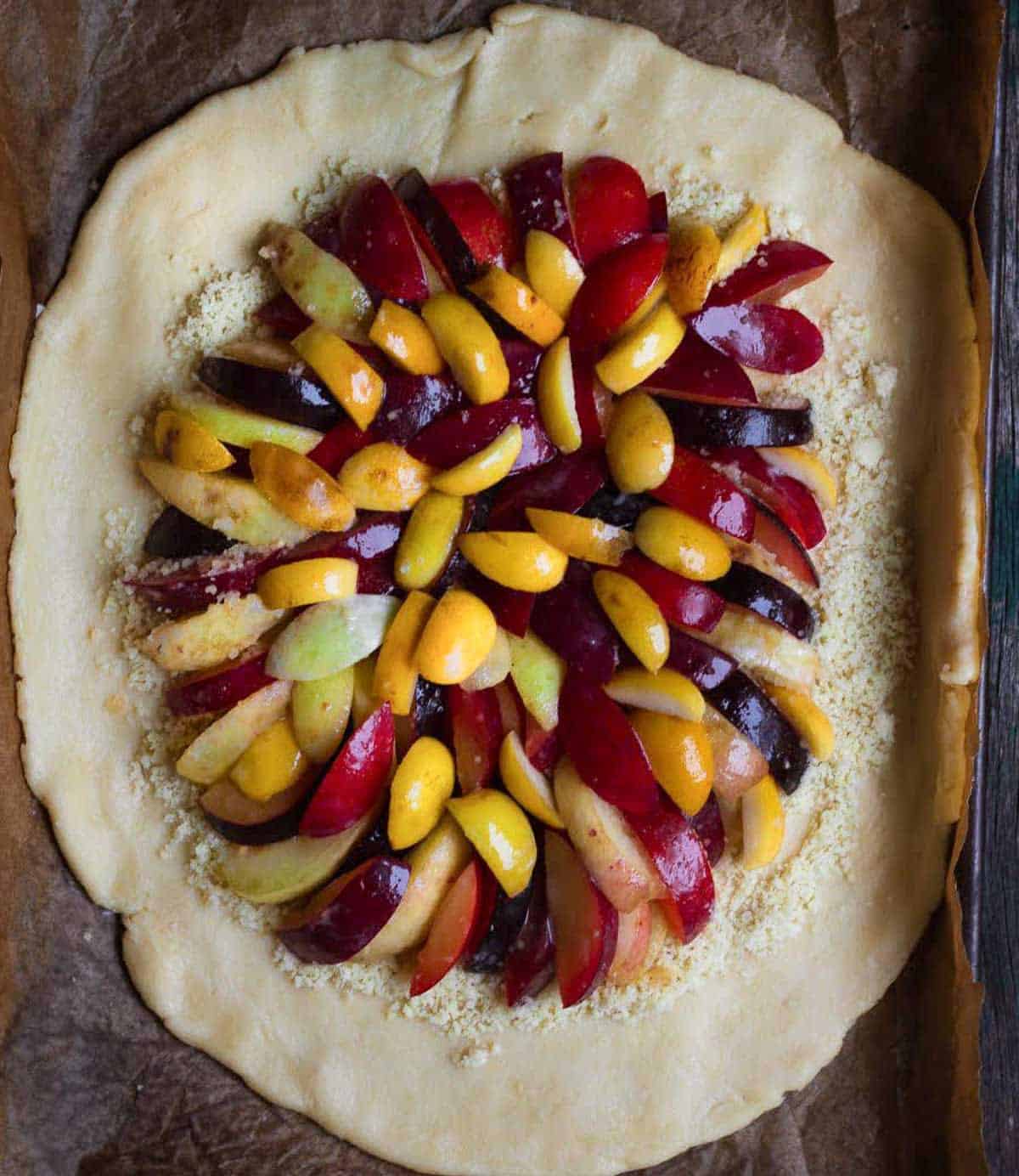 Sliced fruits on top of rolled out pastry dough and almond meal.
