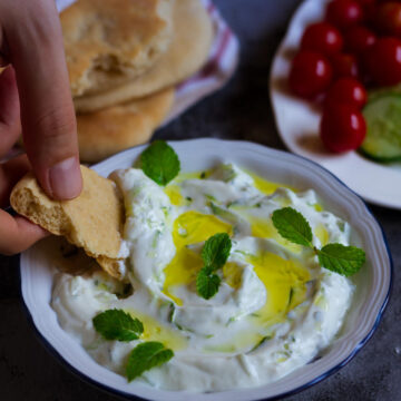 Tzatziki in a bowl with a piece of pita bread scooping it up.