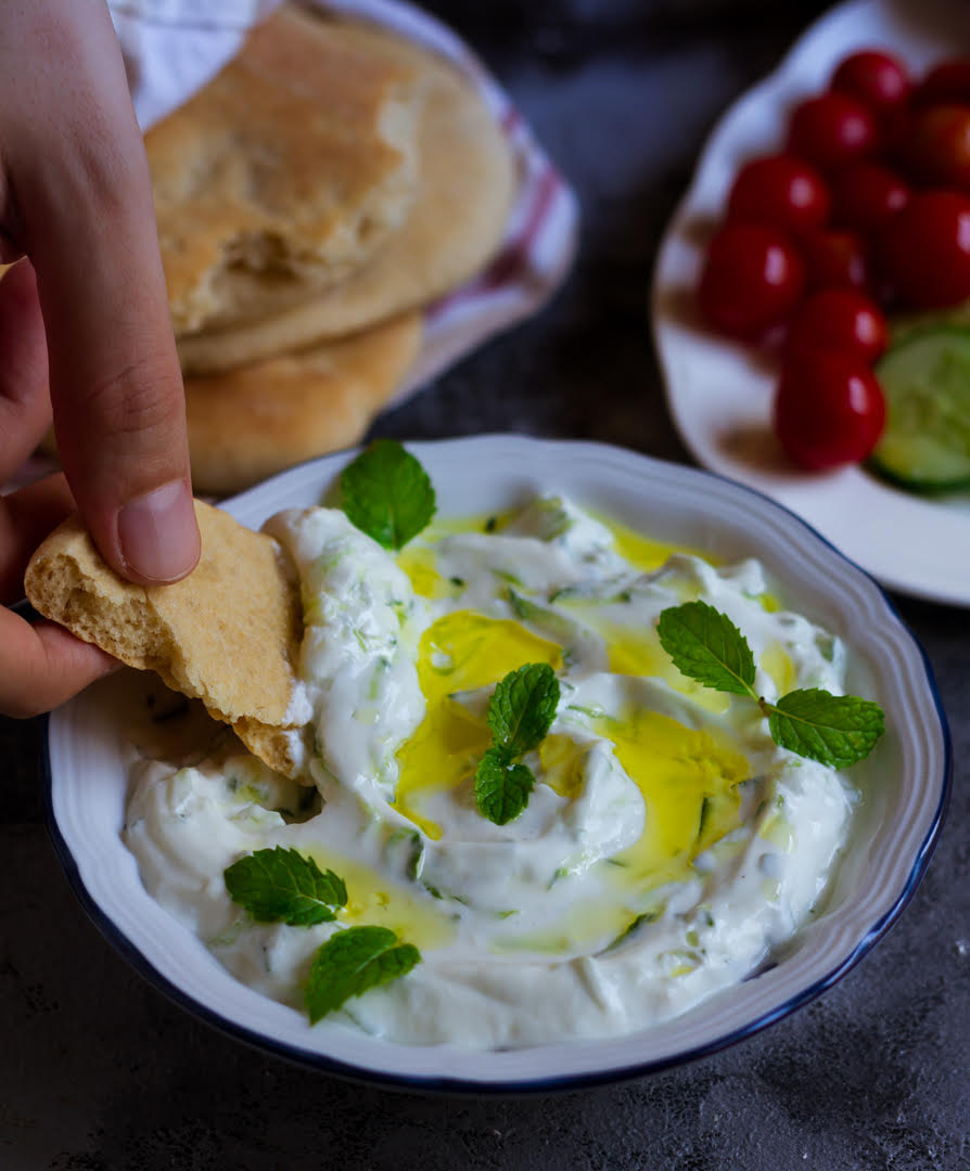 Tzatziki in a bowl with a piece of pita bread scooping it up.