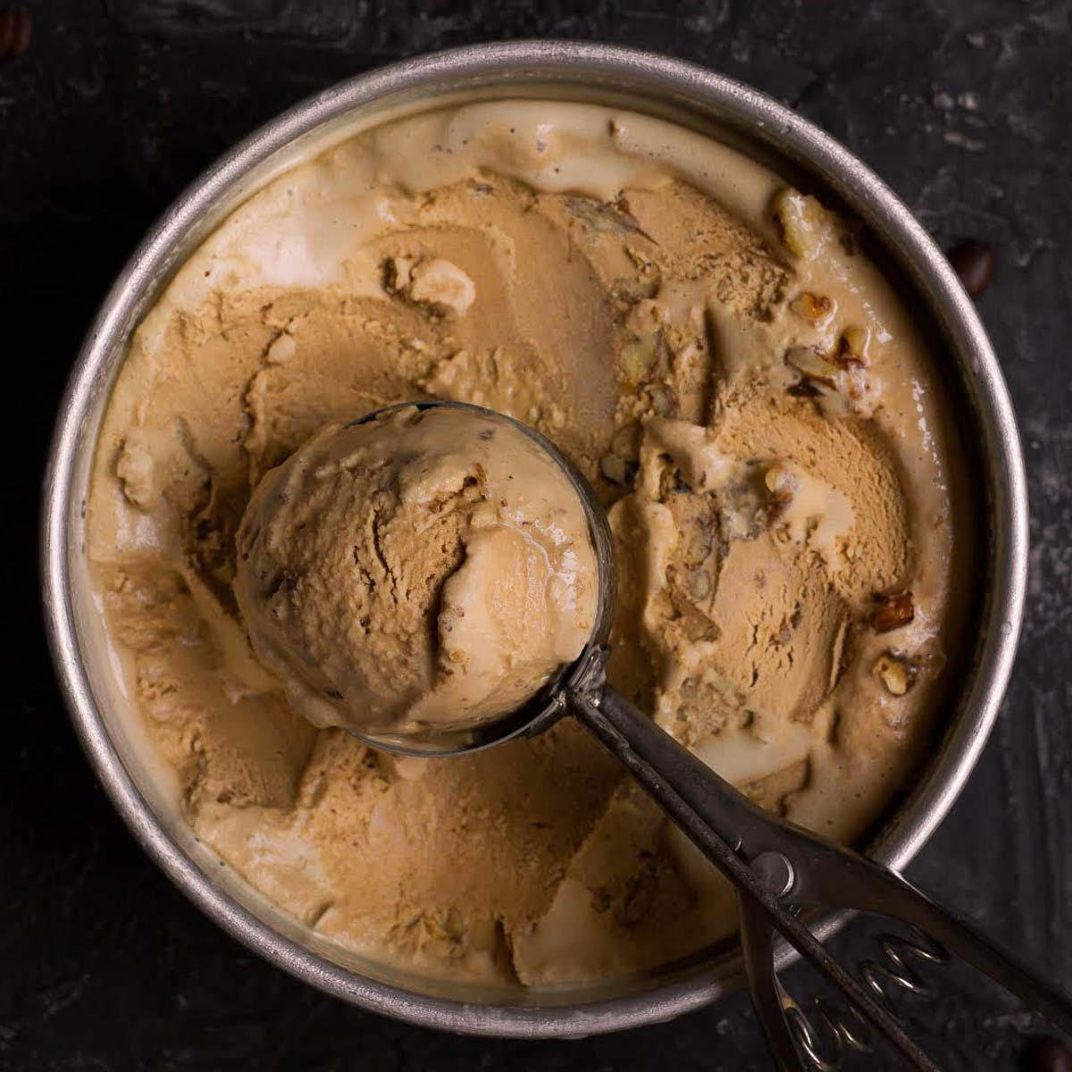 Coffee ice cream in a pan with one scoop in an ice cream scoop.