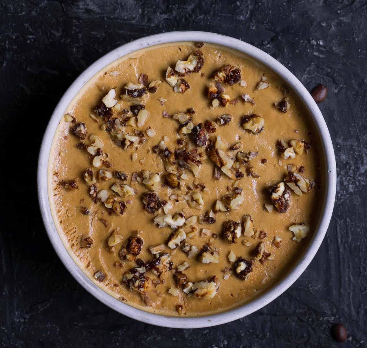 coffee ice cream in a round pan topped with candied walnuts.