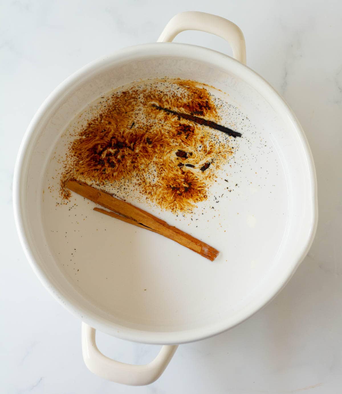 Coconut milk, cream, sugar, coffee powder, vanilla bean and cinnamon stick in a saucepan.