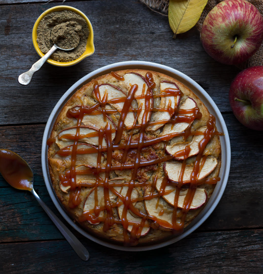 apple cake drizzled with caramel on a wooden board with chai spice and apples.