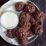 A plate of chocolate cookies with a glass of milk.