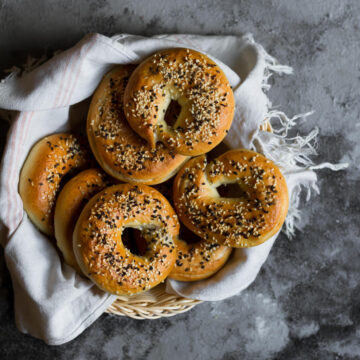 Bagels with sesame seeds in a kitchen towel lined basket.