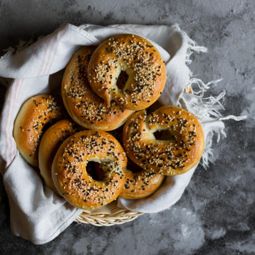 Bagels with sesame seeds in a kitchen towel lined basket.