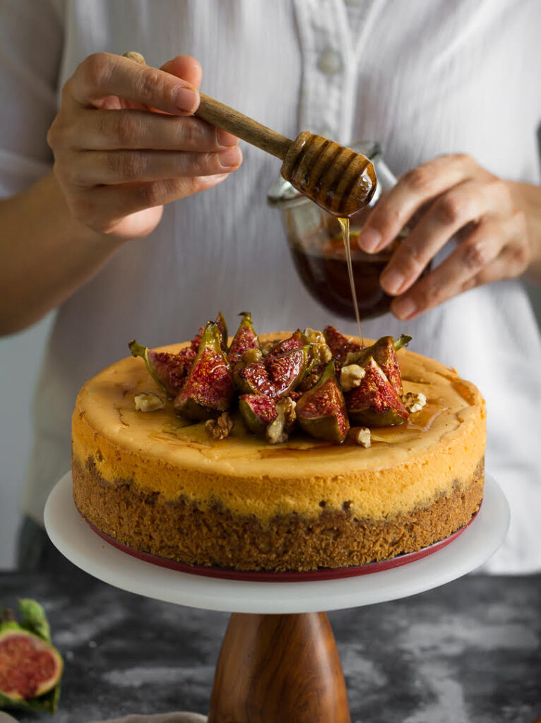 Honey being poured on the cinnamon cheesecake which is topped with figs and walnuts.