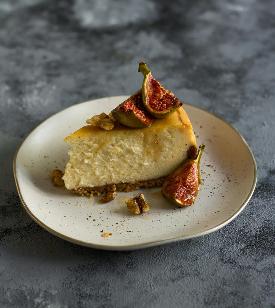 A slice of cheesecake topped with roasted figs and honey on a small plate.