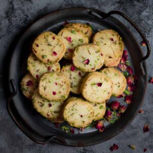 Rose pistachio cookies in a serving tray garnished with dried rose buds.