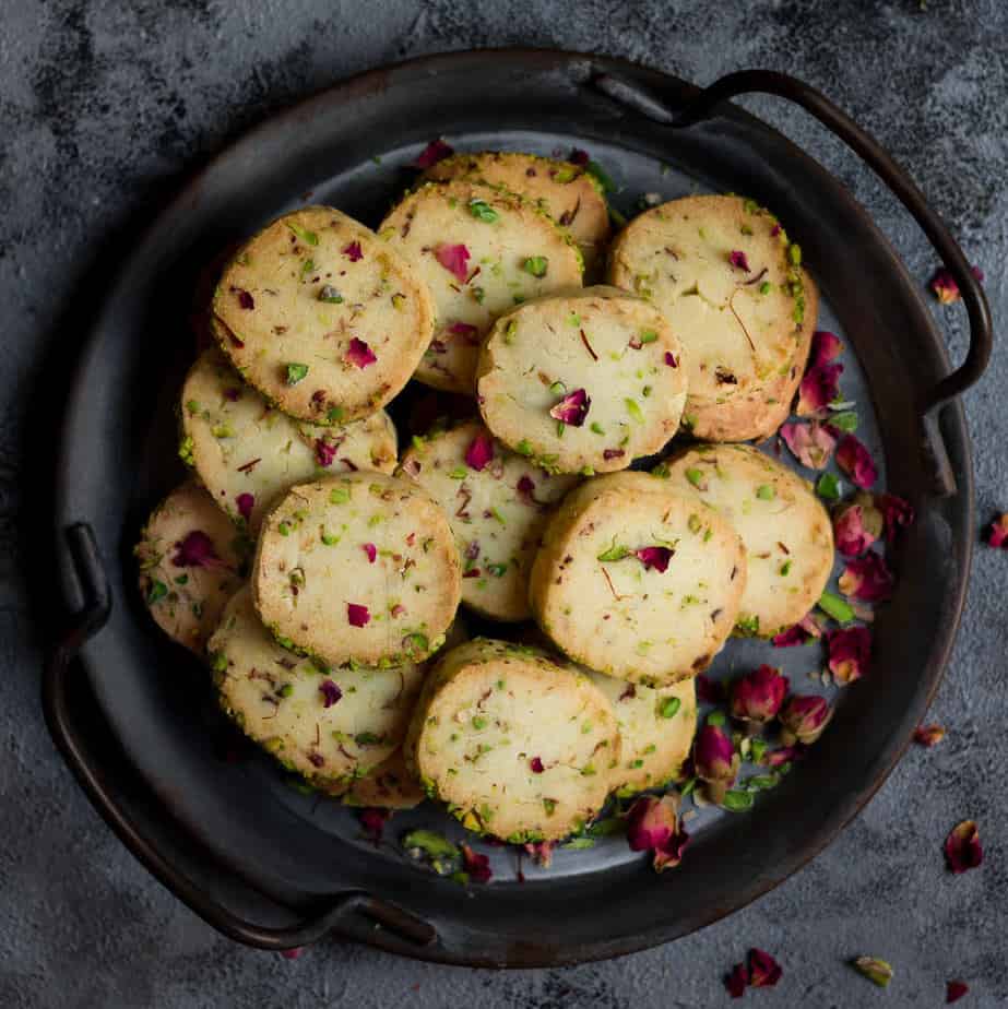 Rose pistachio cookies in a serving tray garnished with dried rose buds.