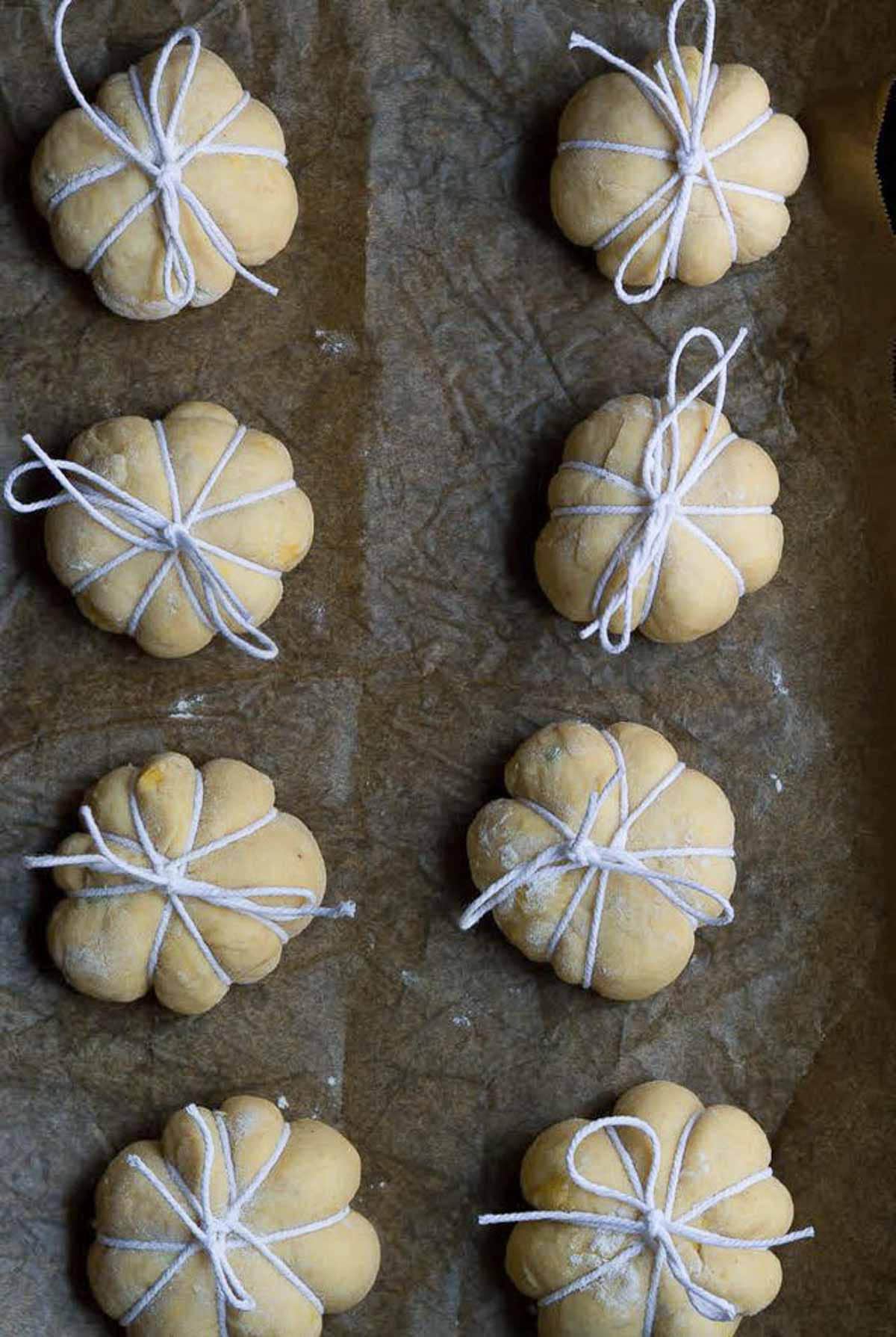 8 dough balls tied up with twine in pumpkin shape on a parchment lined tray.