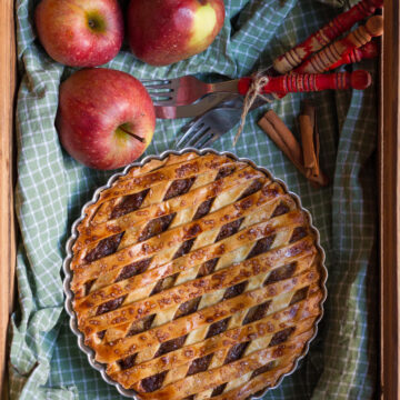 Apple pie in a basket lined with green checked napkin with apples and forks around.
