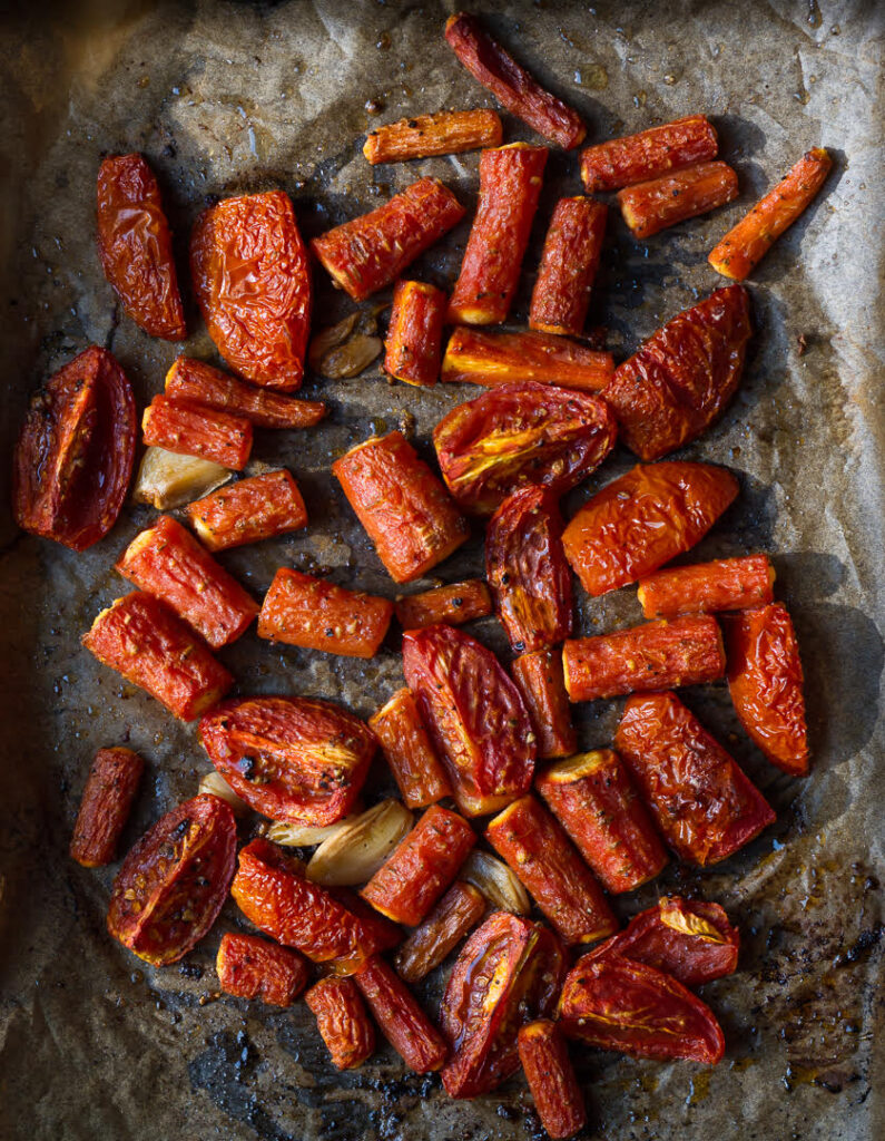 Roasted carrots, tomatoes, and garlic on a baking tray.