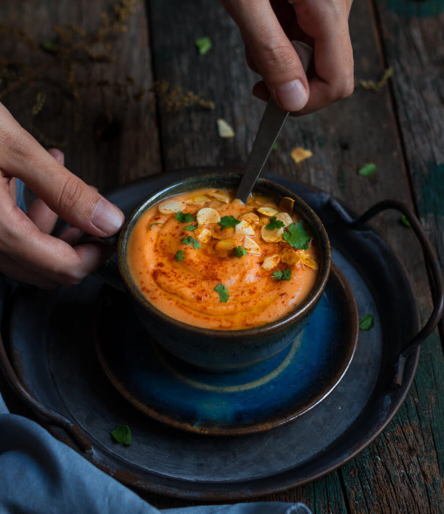 a hand holding a spoon and the bowl of soup.
