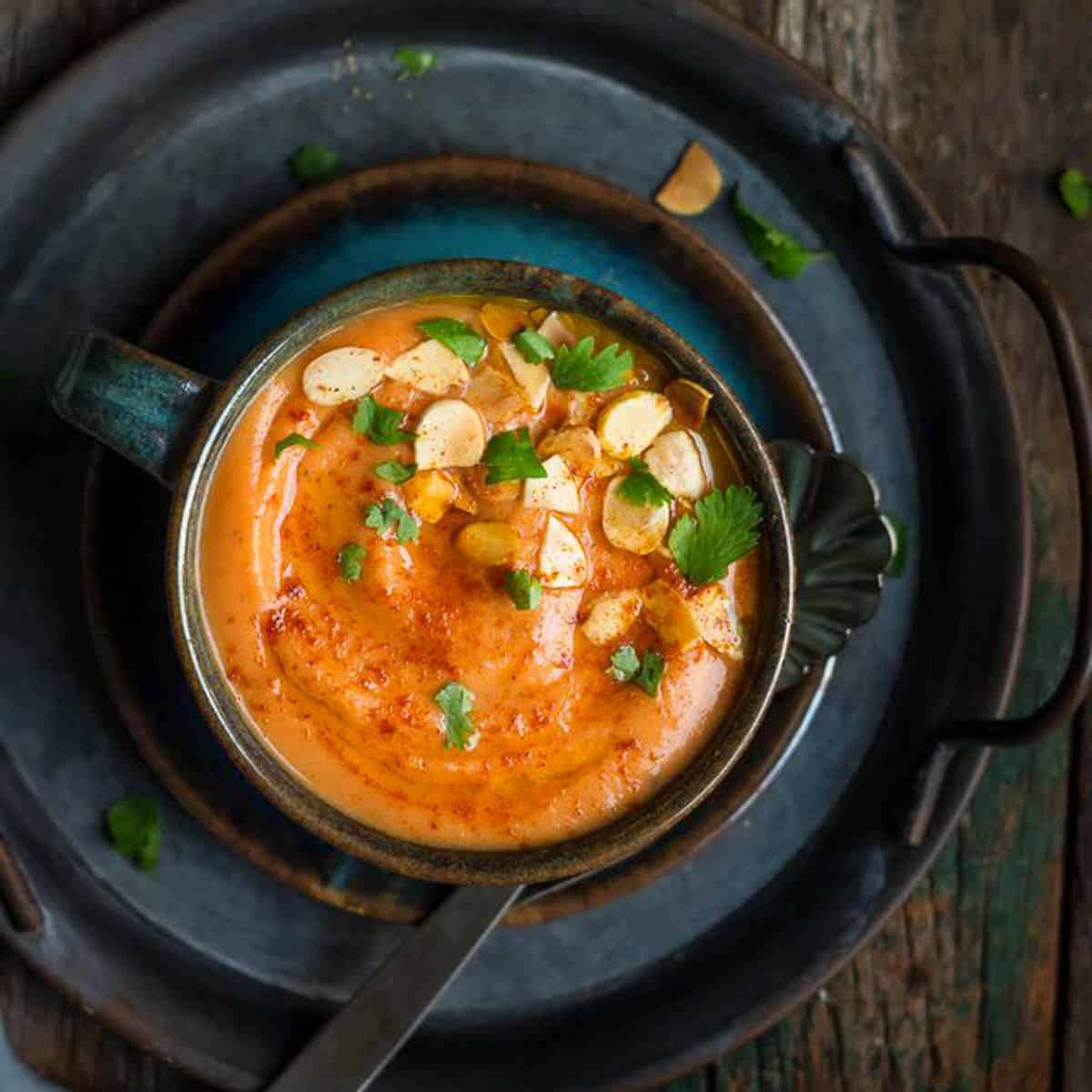 A bowl of roasted carrot soup garnished with almonds on a tray.
