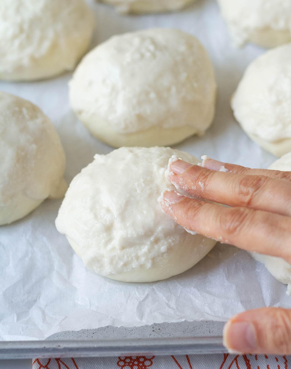 A hand coating a paste on top of a dough ball.