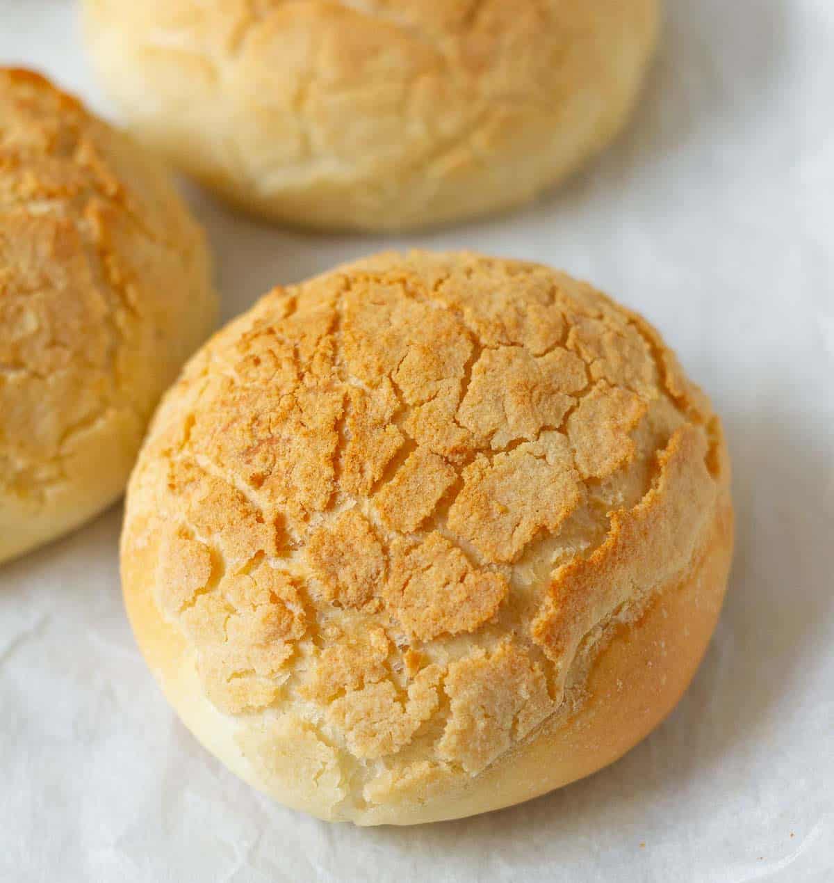 A bread roll with crackled crust on parchment paper.