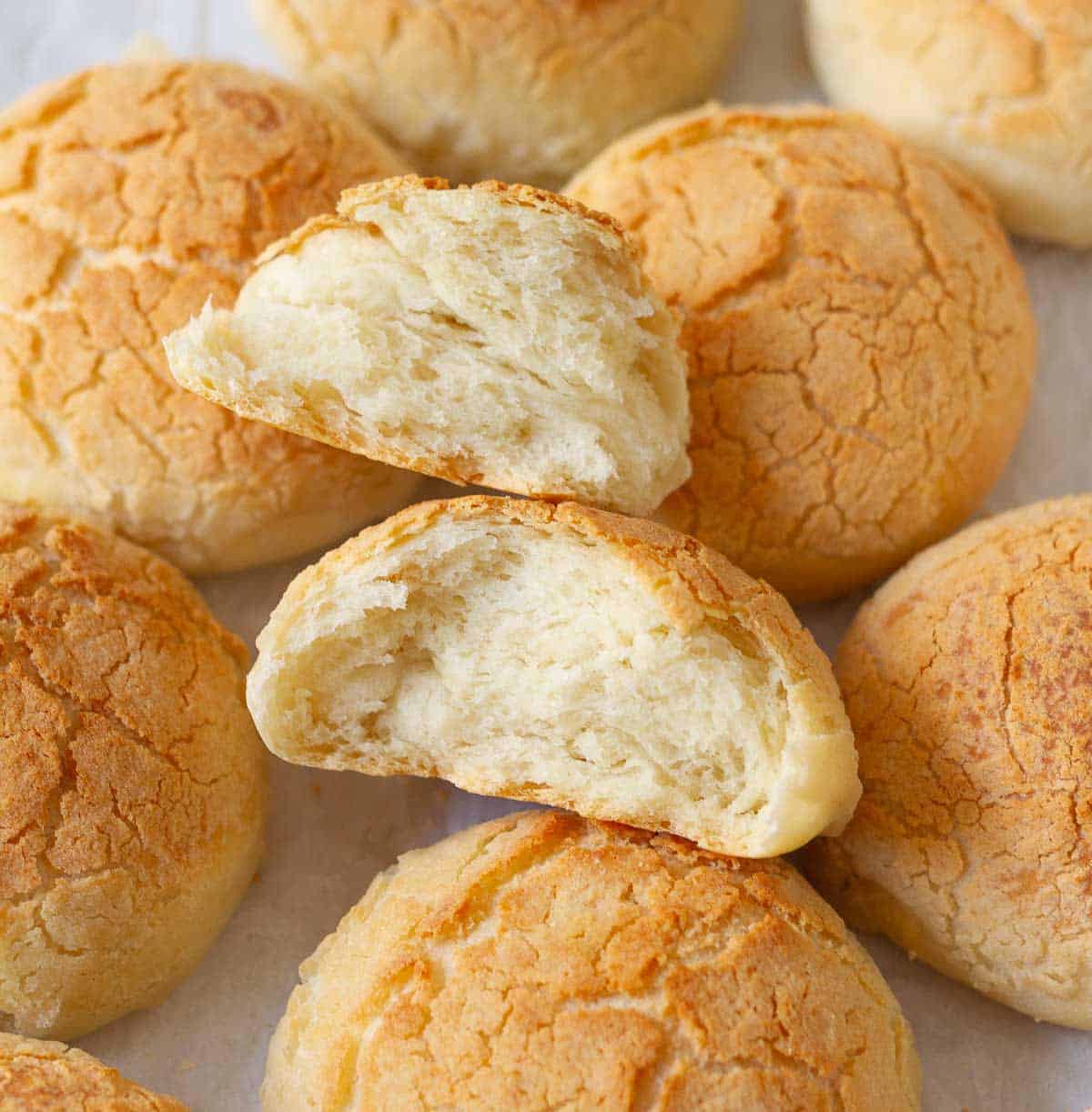 A bread roll split in half with more bread rolls on parchment paper.