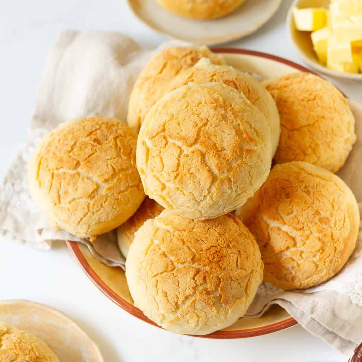 Bread rolls stacked in a bowl with butter on the side.