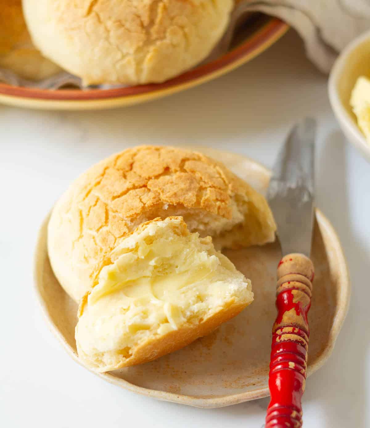 A bread roll split in half and buttered with a knife on the side.