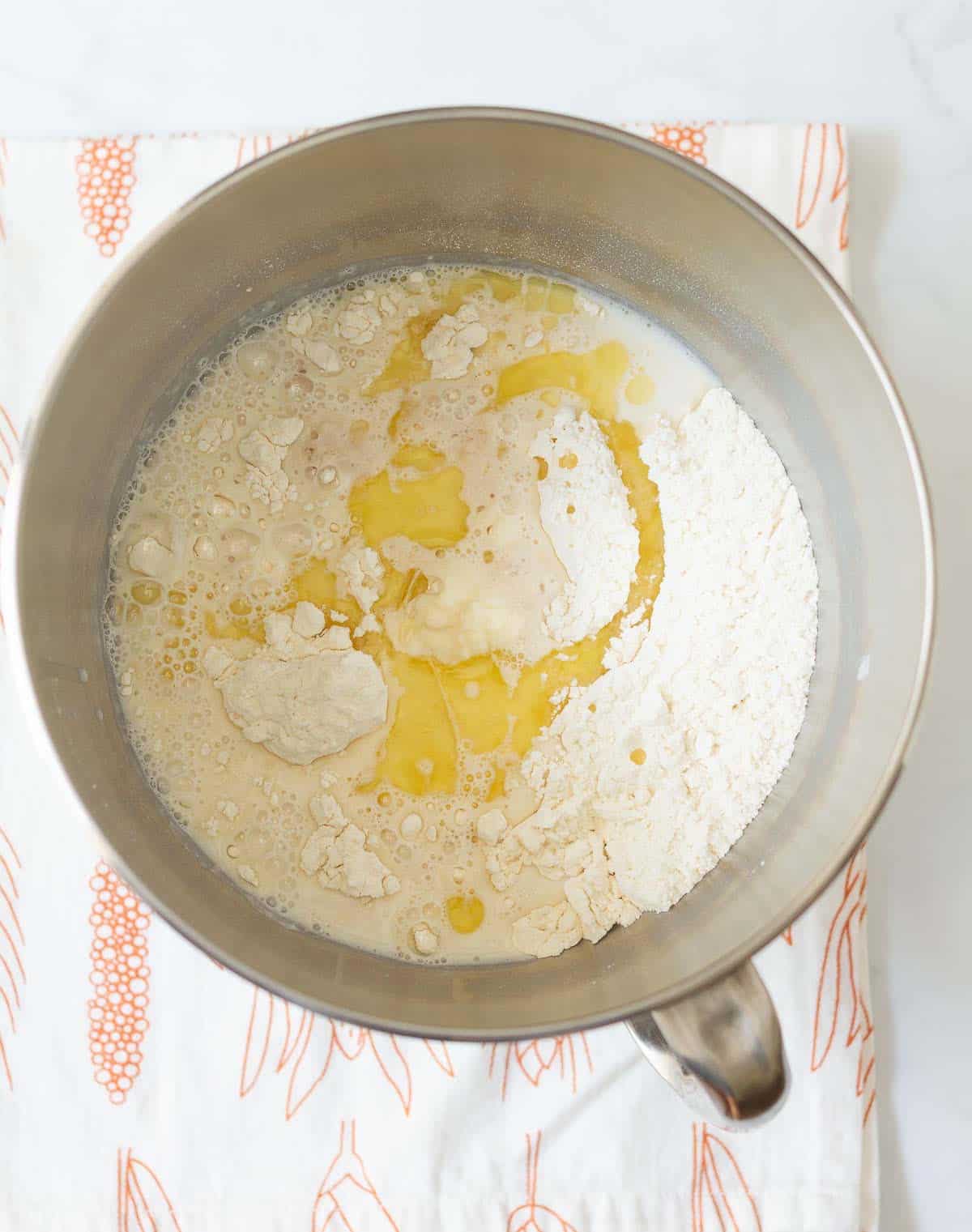 Flour, olive oil, and yeast mixture in a stand mixer bowl.
