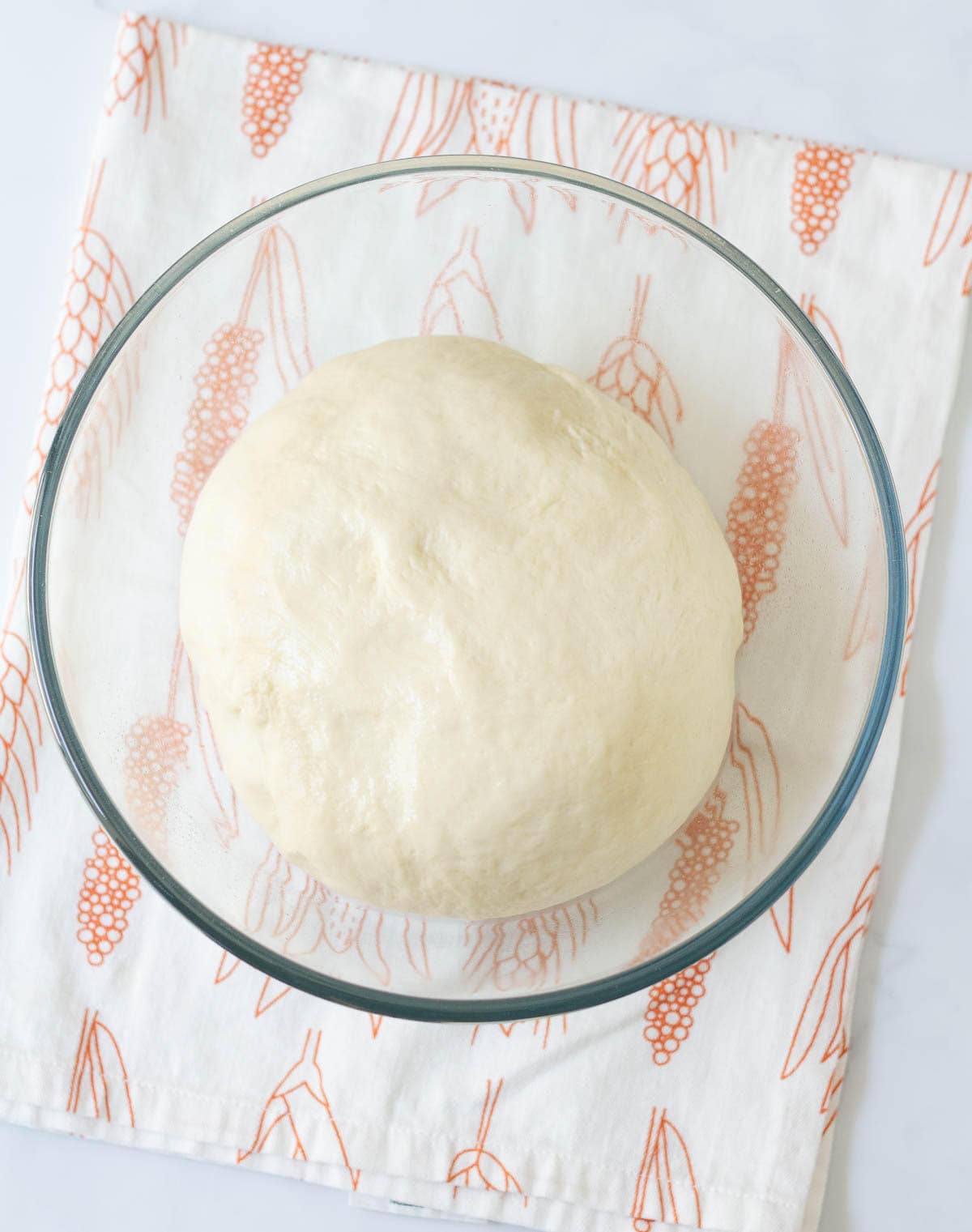 Dough in a glass bowl on a kitchen towel.
