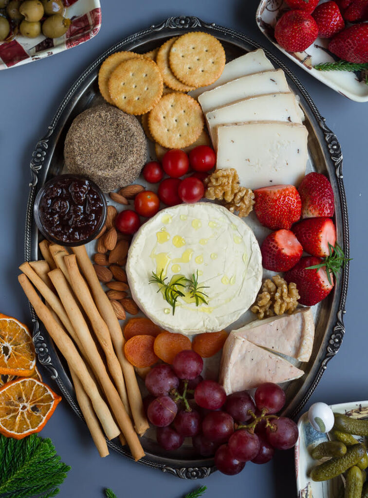 cheese, fruits, nuts, crackers, breadsticks,jam on a silver platter.
