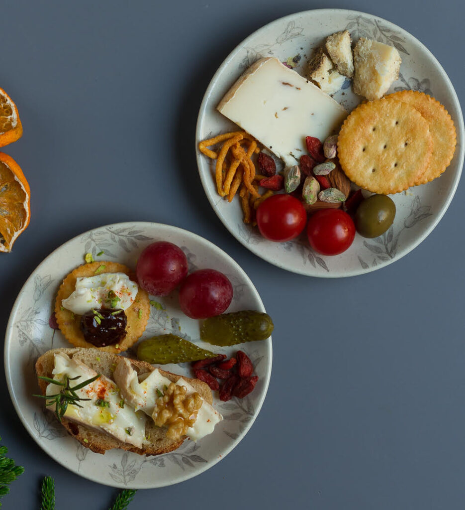 cheese, crackers, bread with nuts and vegetables on 2 small plates.