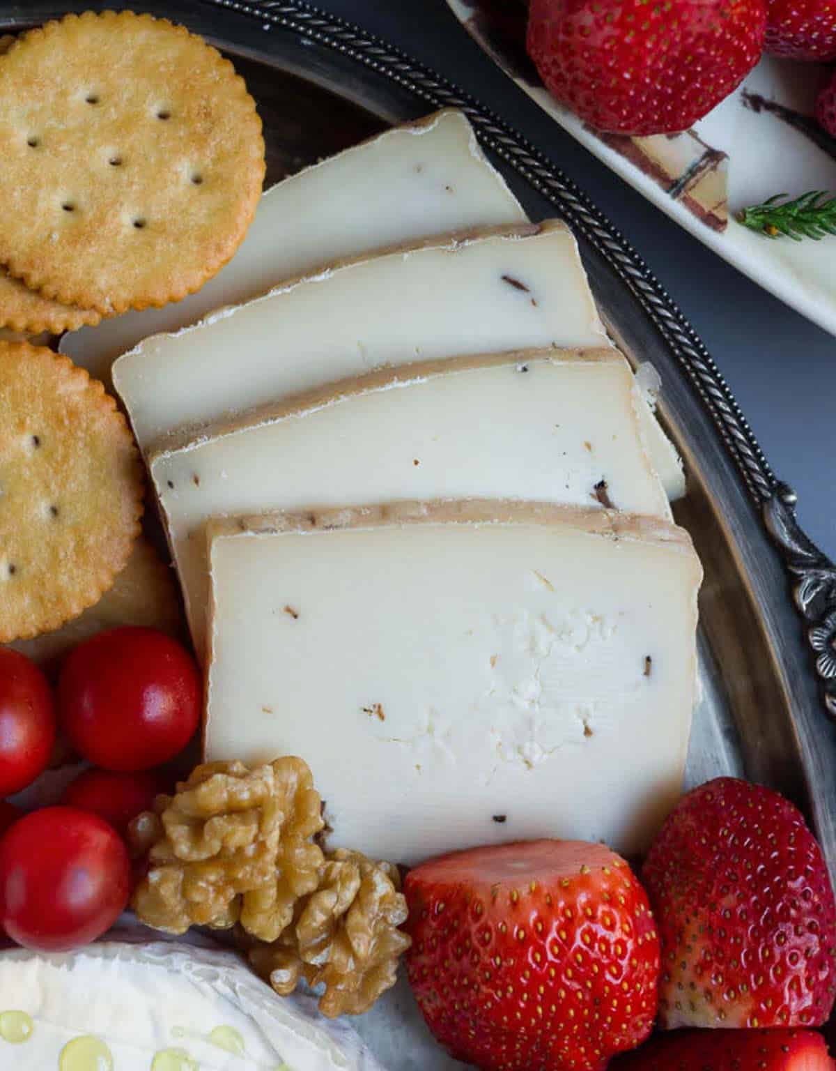 Mushroom truffle cheese with crackers, fruits and nuts on a platter.