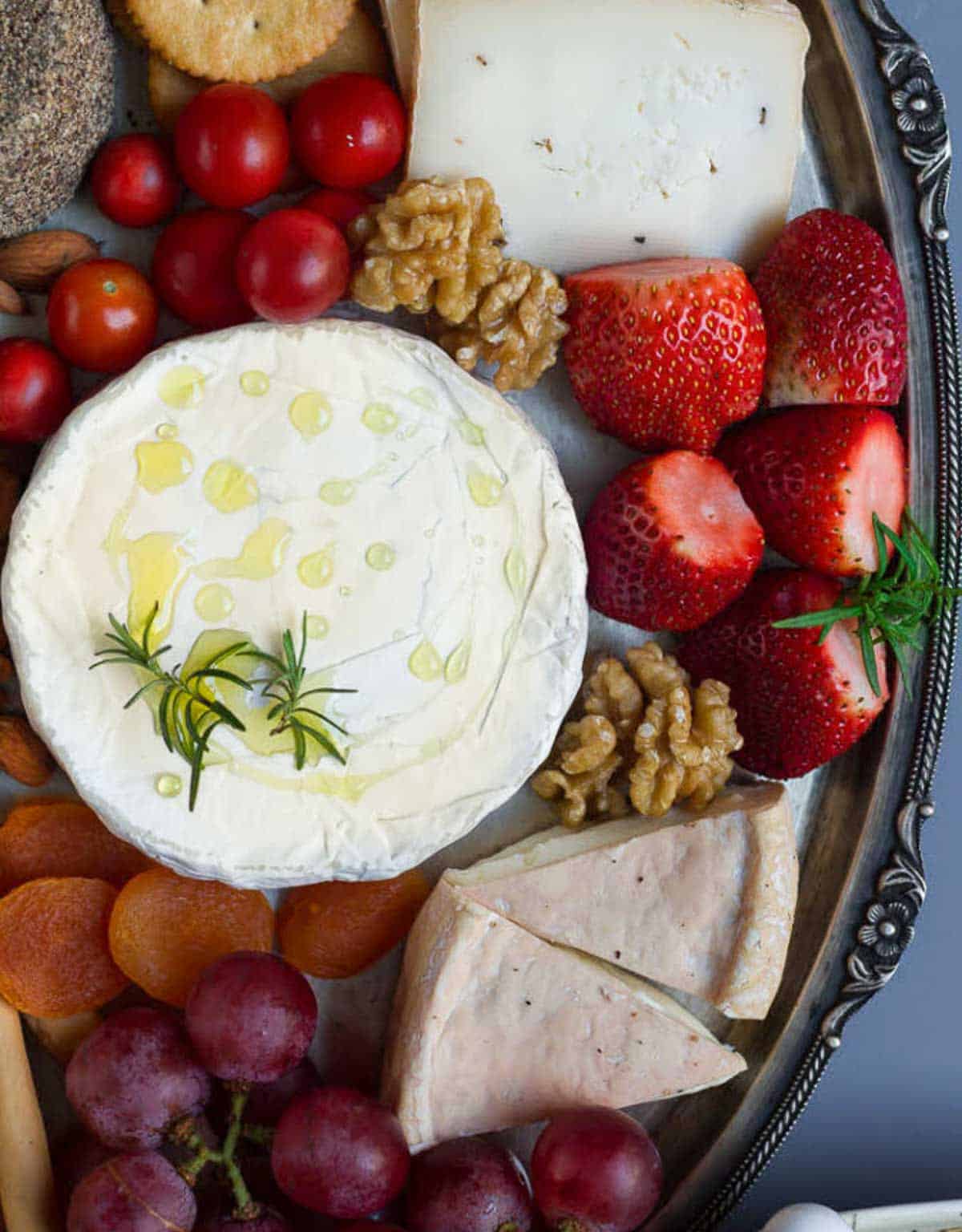 camembert cheese with strawberries, nuts, cherry tomatoes on a platter.