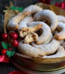 A tin full of crescent-shaped cookies with 1 cookie broken in half.