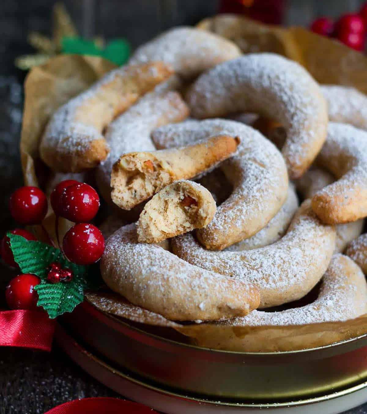 A tin full of crescent-shaped cookies with 1 cookie broken in half.