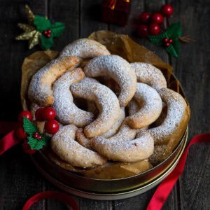 Lemon crescent cookies in a tin box with christmas decorations around.