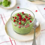 matcha chia pudding in a glass cup topped with pomegranates and chocolate bits.