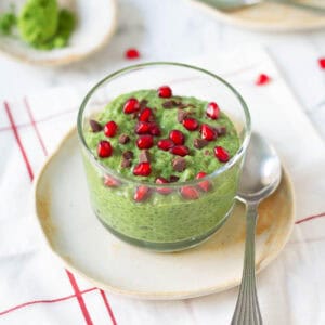 matcha chia pudding in a glass cup topped with pomegranates and chocolate bits.