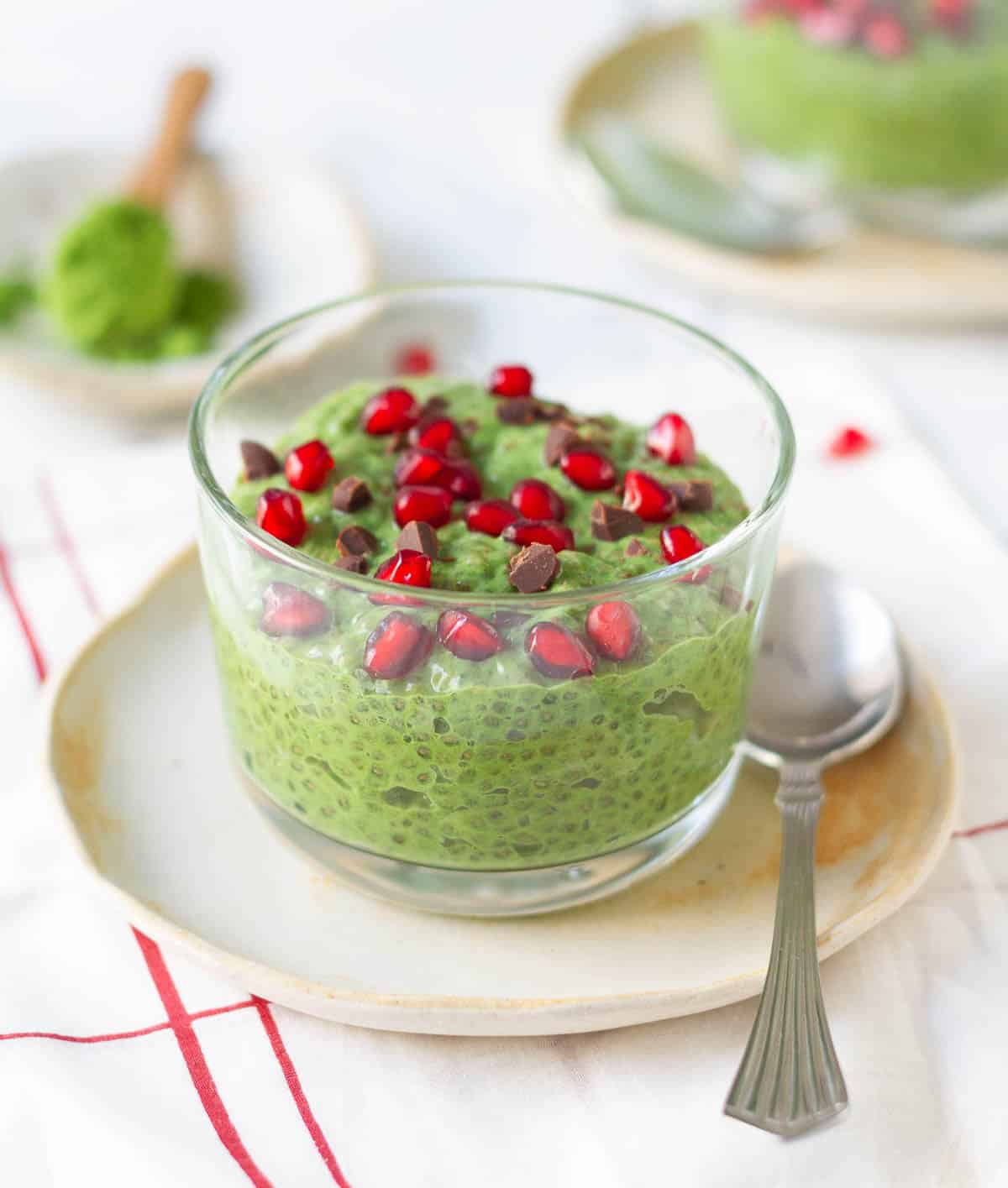 matcha chia pudding in a glass cup on a small plate with a spoon.
