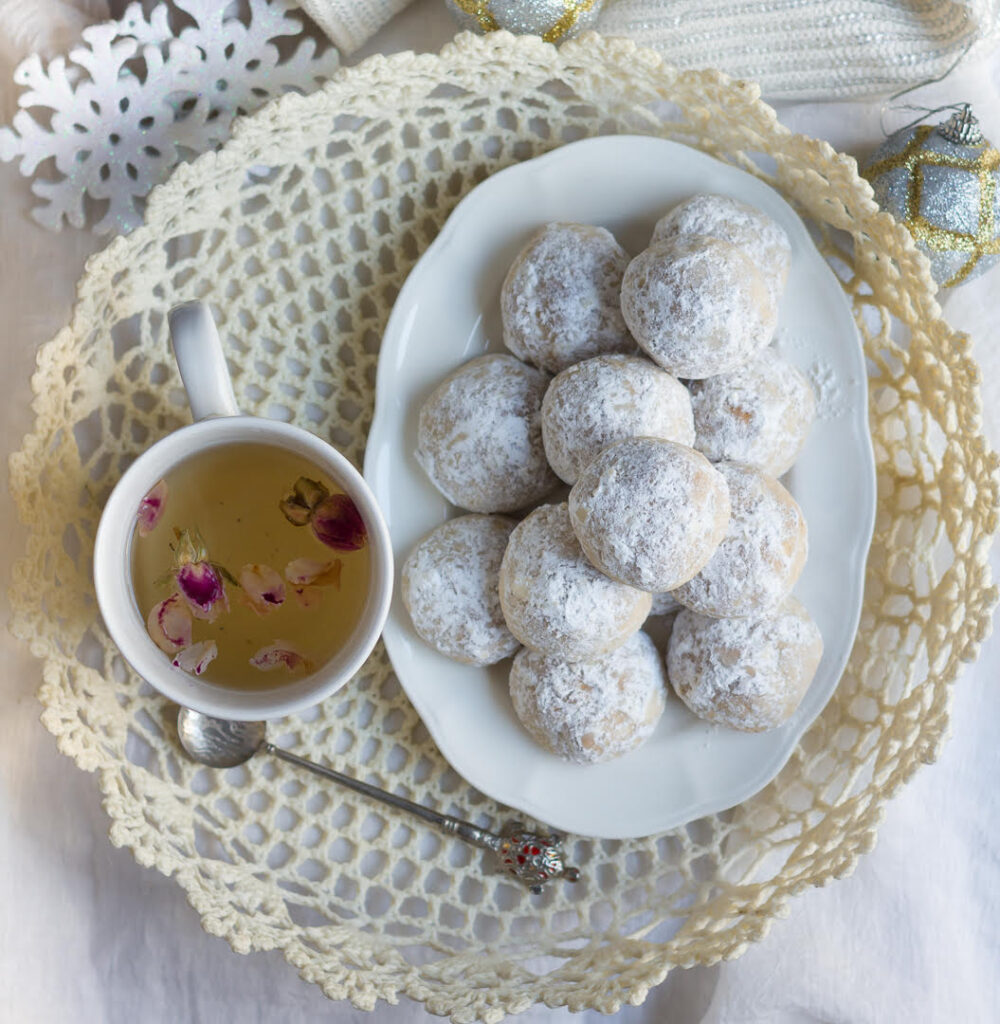 a cup of herbal tea next to a platter of christmas cookies on a white platter.