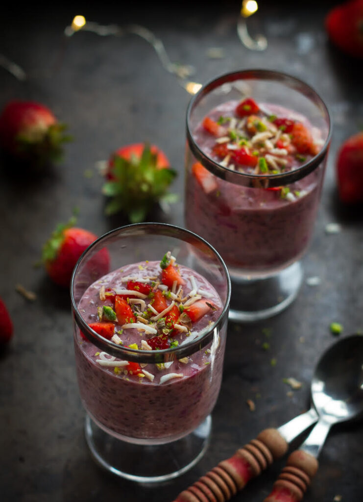 chia pudding with strawberries in 2 dessert glasses on a black tray.