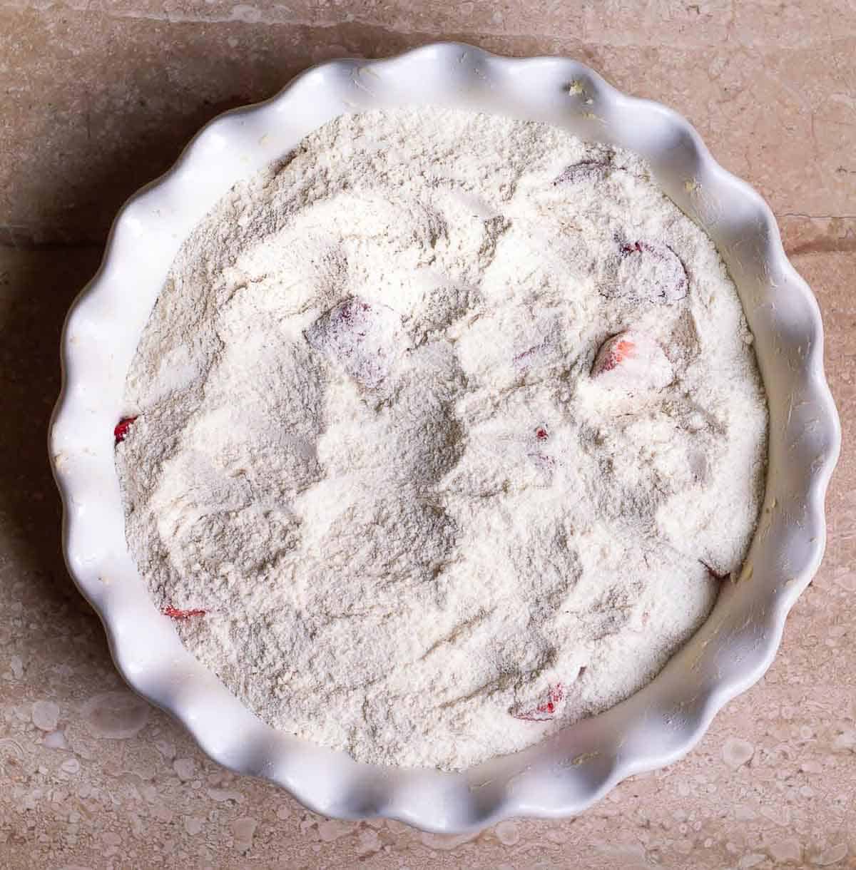 dry ingredients on top of the strawberries in a baking dish.
