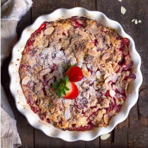 strawberry dump cake in a round baking dish topped with almonds and fresh strawberries.