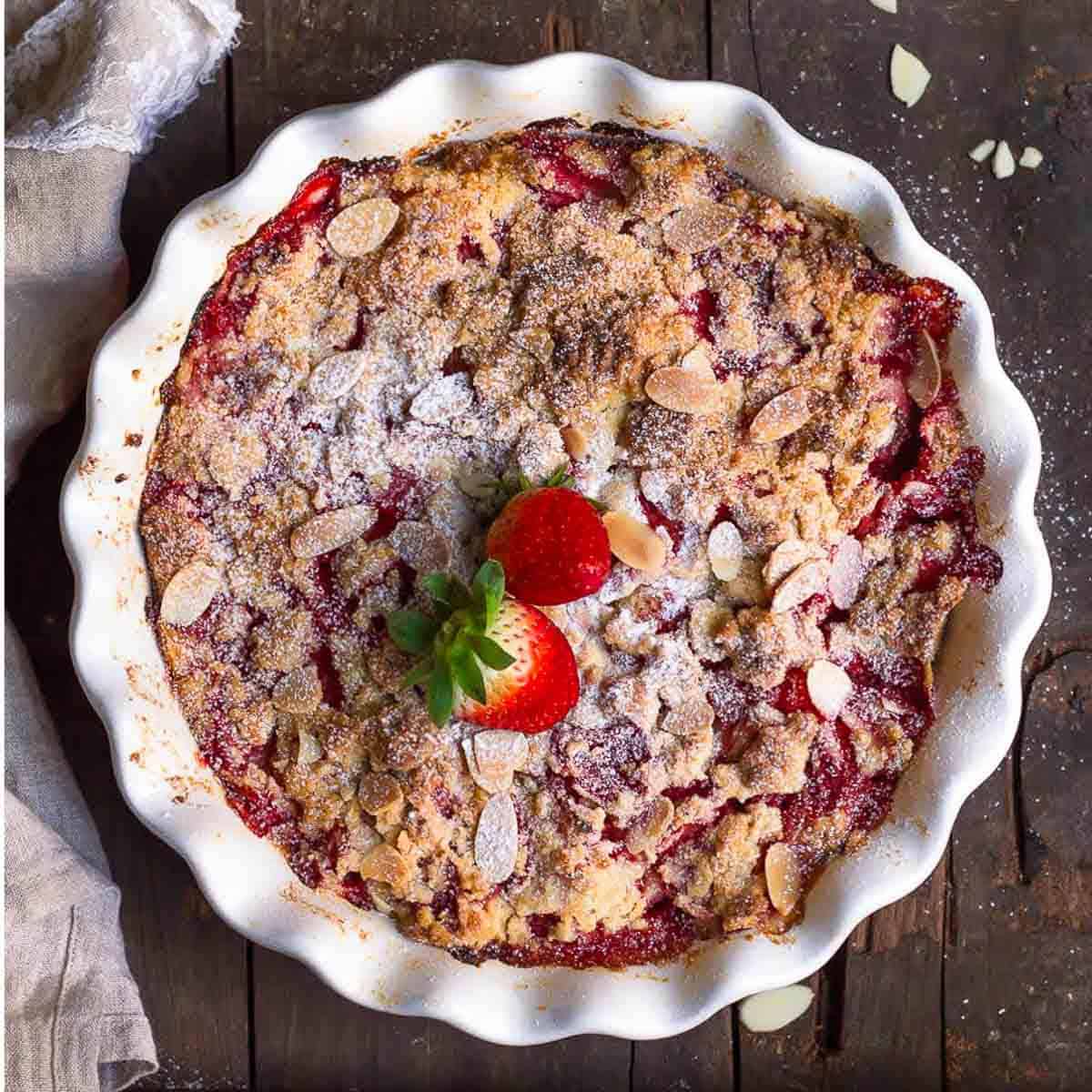 strawberry dump cake in a round baking dish topped with almonds and fresh strawberries.