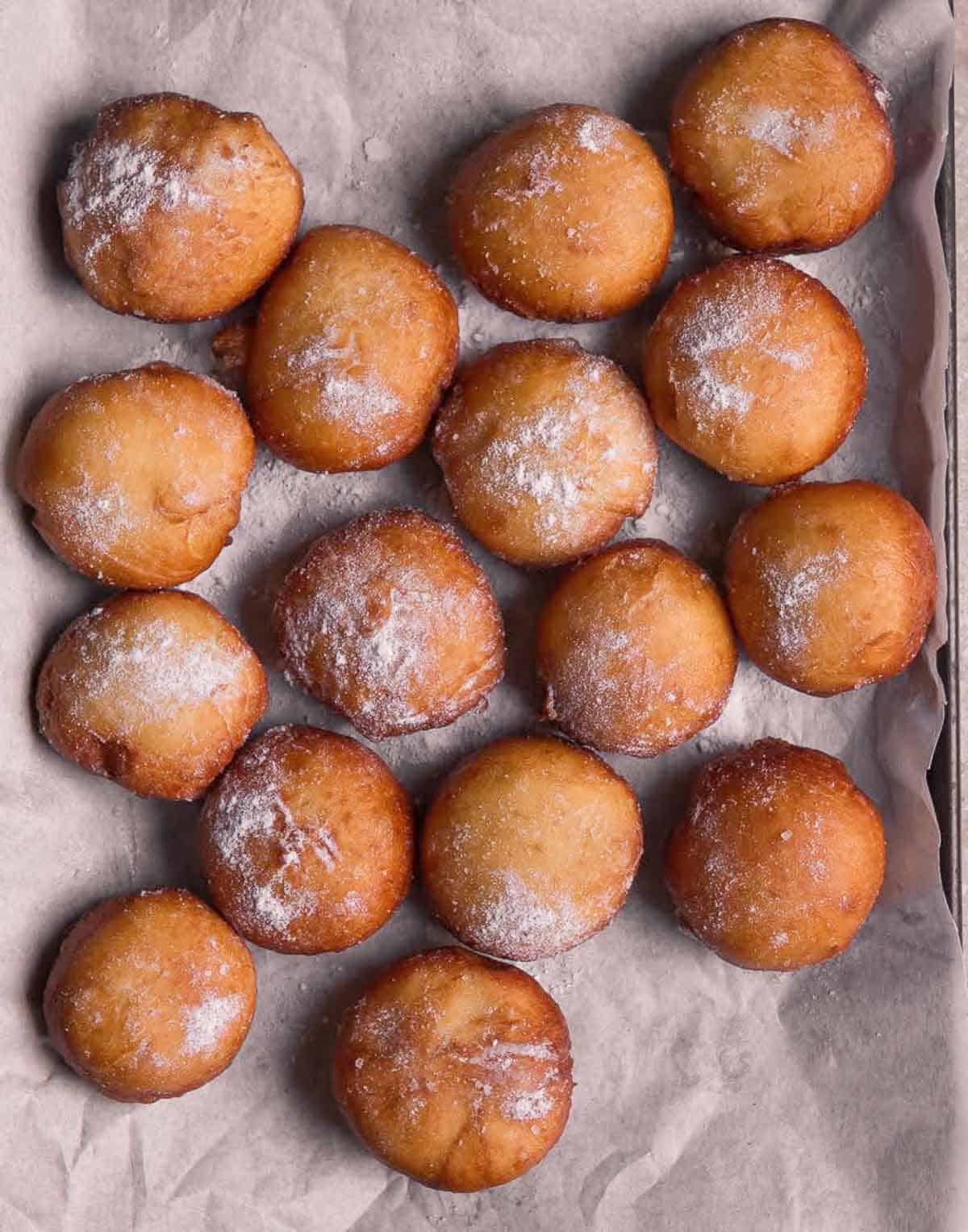 Fried donuts dusted with sugar on a parchment-lined tray.