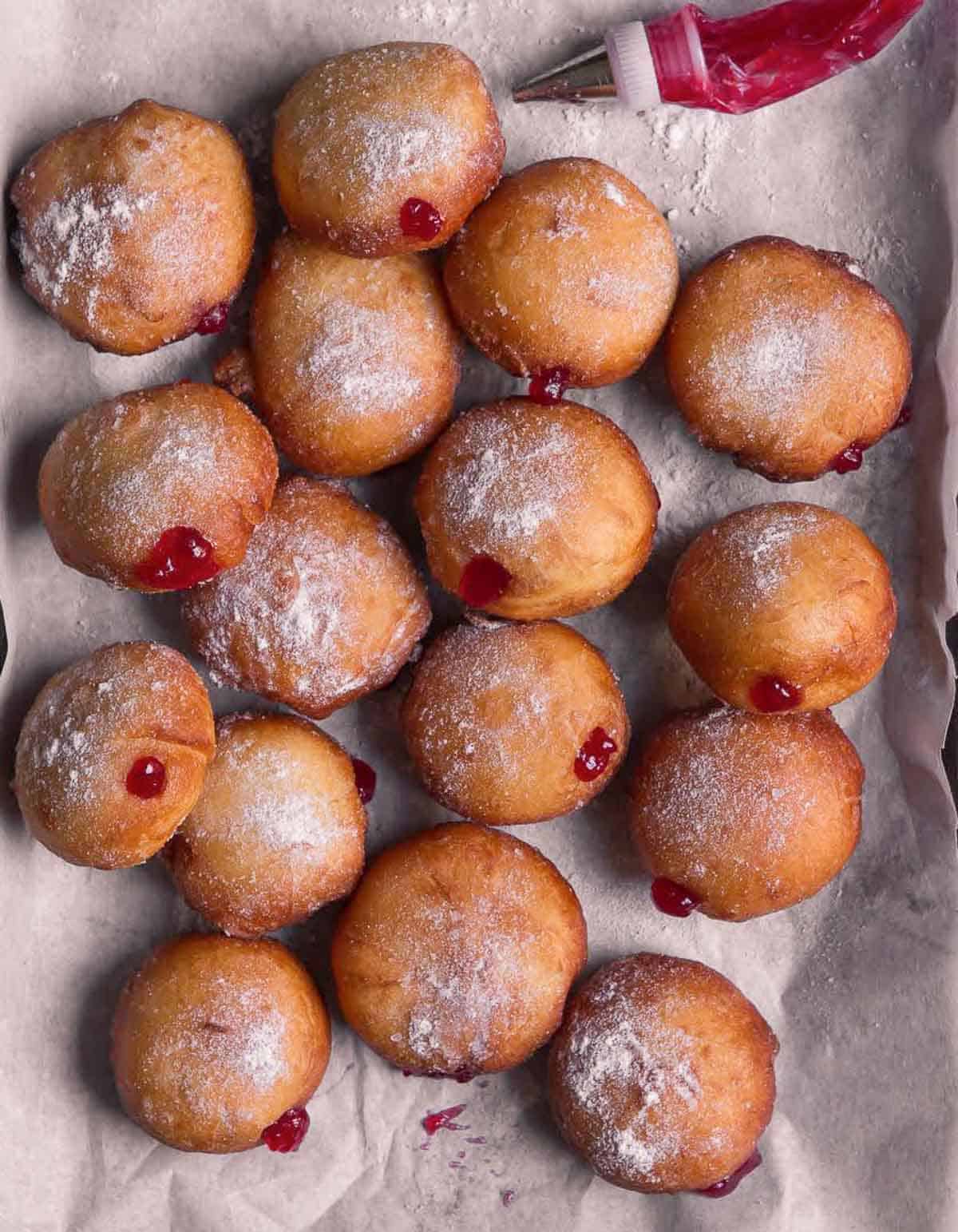donuts filled with strawberry jam on a tray with a jam-filled piping bag on the side.